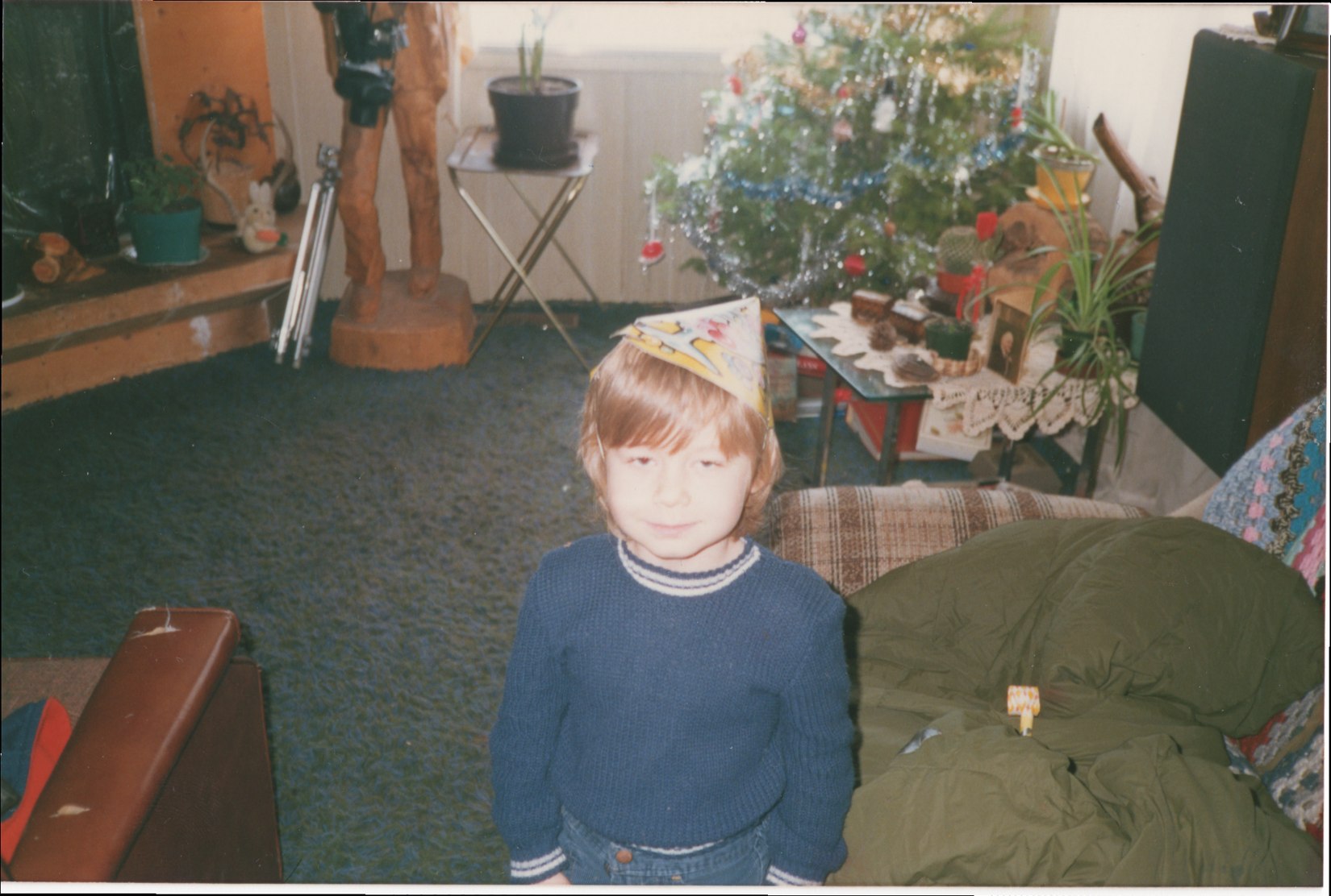 Young child wearing a paper hat near a Christmas tree